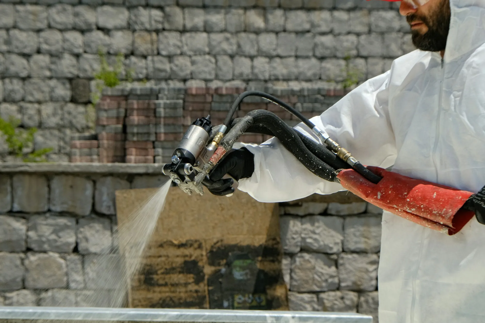 Worker in a protective suit spraying water to keep material wet